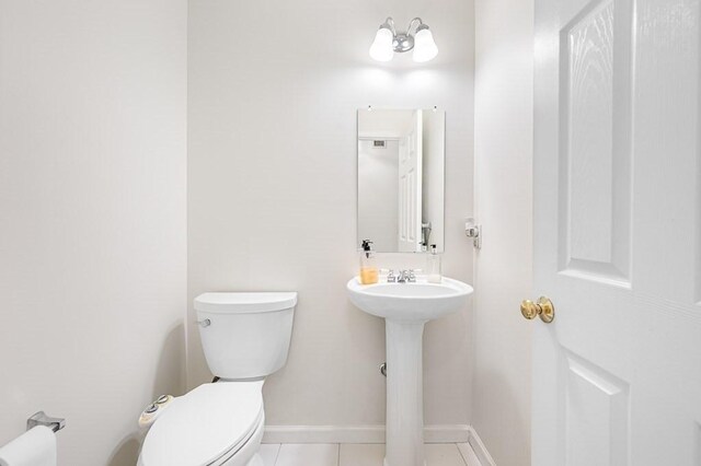 half bathroom with toilet, tile patterned floors, baseboards, and a sink