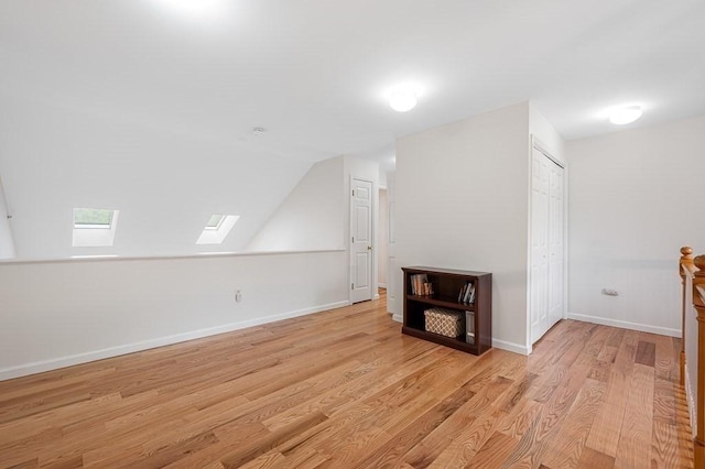 bonus room with a skylight, light wood-style floors, baseboards, and vaulted ceiling