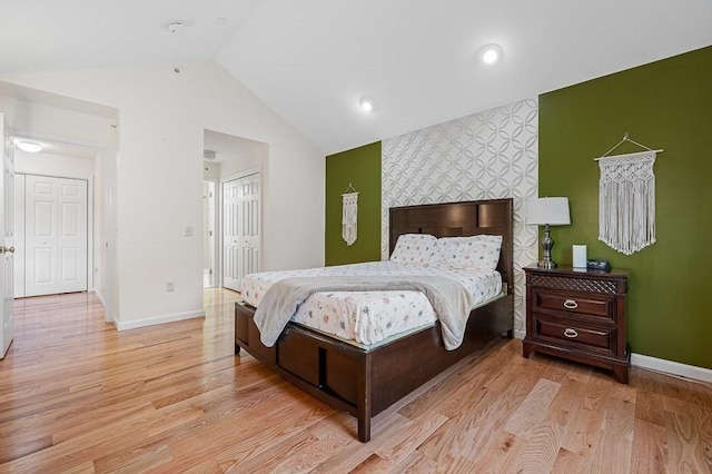 bedroom with an accent wall, lofted ceiling, baseboards, light wood-style flooring, and a closet