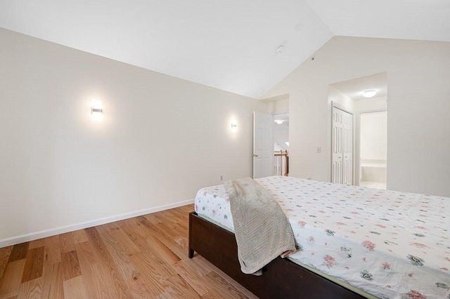 bedroom featuring light wood finished floors, ensuite bath, baseboards, and high vaulted ceiling