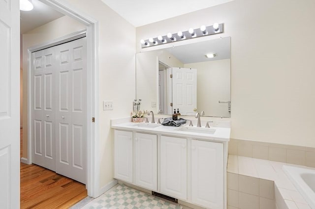 full bath with double vanity, tiled tub, and wood finished floors