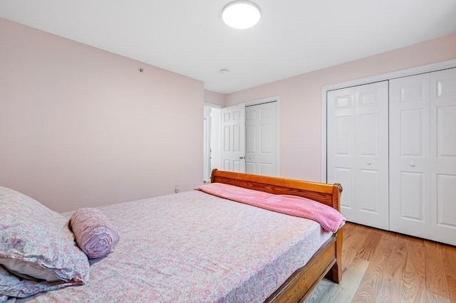 bedroom featuring light wood finished floors and multiple closets