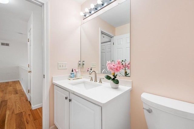 half bath featuring wood finished floors, toilet, and vanity