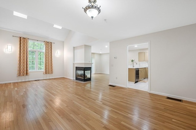 unfurnished living room featuring light wood-style flooring, a multi sided fireplace, baseboards, lofted ceiling, and a sink