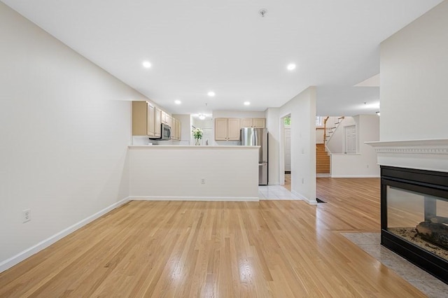 unfurnished living room with baseboards, light wood finished floors, stairway, and recessed lighting