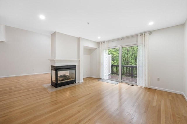 unfurnished living room featuring baseboards, a multi sided fireplace, light wood-type flooring, and recessed lighting