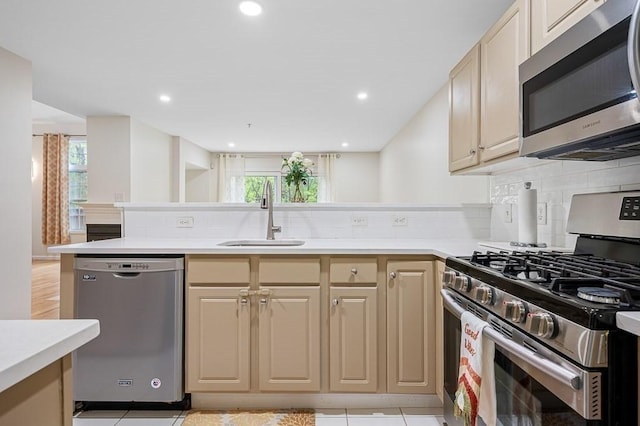 kitchen with appliances with stainless steel finishes, a sink, a peninsula, light countertops, and recessed lighting
