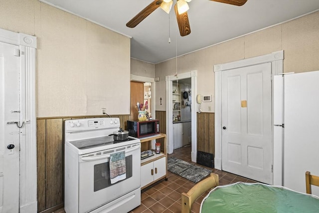 kitchen with ceiling fan, white appliances, dark tile patterned floors, and wood walls