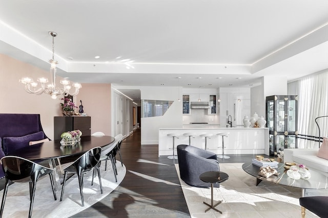 dining space with a notable chandelier, sink, light hardwood / wood-style floors, and a raised ceiling