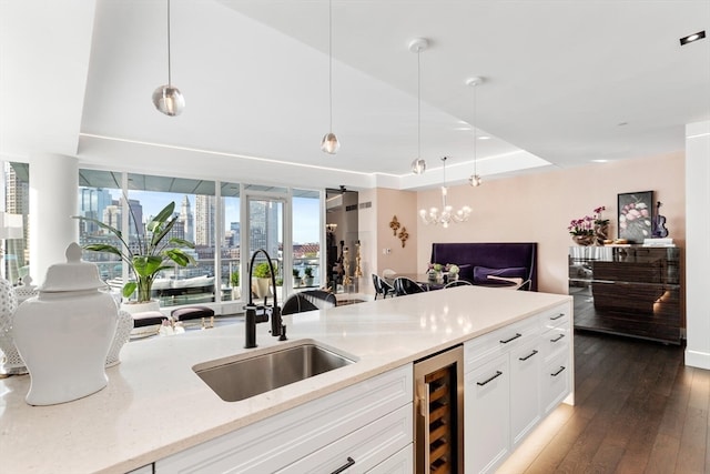 kitchen with light stone counters, wine cooler, hanging light fixtures, sink, and dark hardwood / wood-style floors