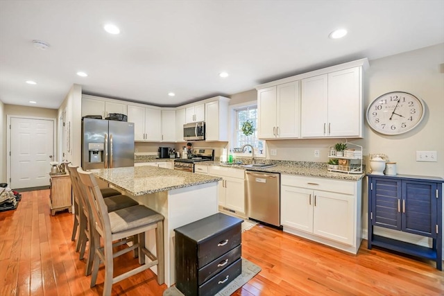 kitchen with white cabinets, appliances with stainless steel finishes, light wood-type flooring, and a kitchen island