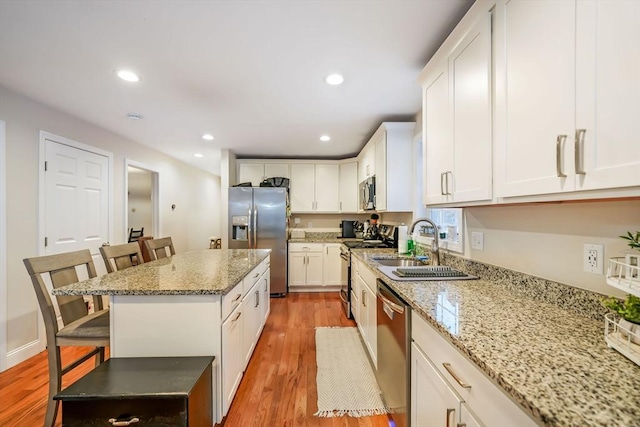 kitchen featuring a kitchen bar, appliances with stainless steel finishes, white cabinets, a kitchen island, and light hardwood / wood-style flooring