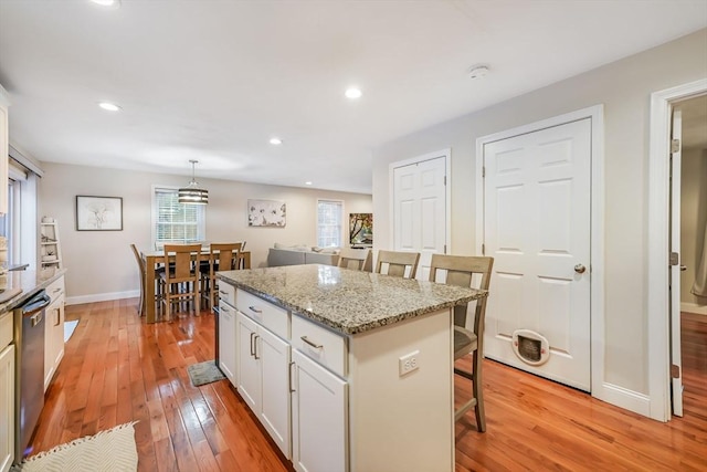 kitchen featuring a breakfast bar area, white cabinets, hanging light fixtures, light stone counters, and a center island