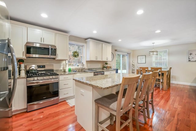 kitchen with appliances with stainless steel finishes, white cabinets, pendant lighting, light hardwood / wood-style flooring, and a center island