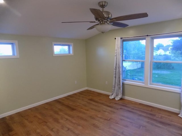 empty room with healthy amount of natural light, wood finished floors, ceiling fan, lofted ceiling, and baseboards