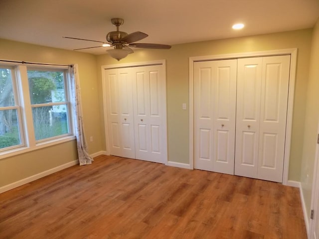 unfurnished bedroom featuring two closets, baseboards, light wood finished floors, recessed lighting, and a ceiling fan