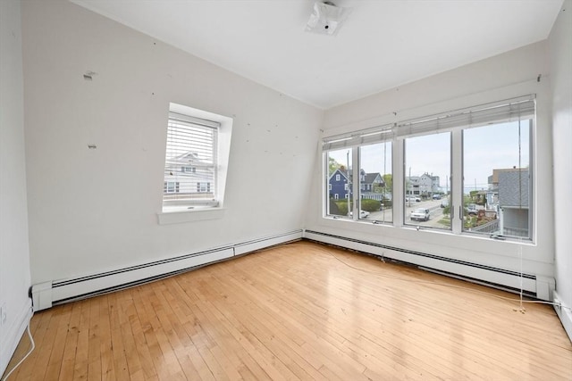 empty room featuring wood-type flooring, a baseboard heating unit, and a healthy amount of sunlight