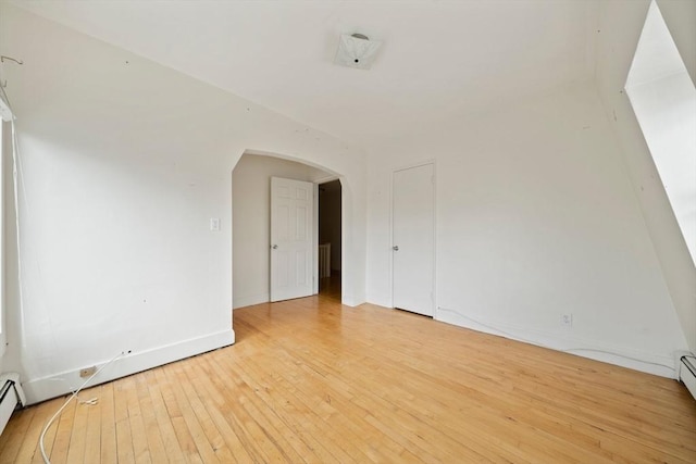 empty room with baseboards, light wood-style flooring, a baseboard radiator, and arched walkways