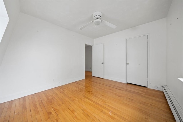 unfurnished bedroom featuring a baseboard heating unit, light wood-style floors, a ceiling fan, and baseboards