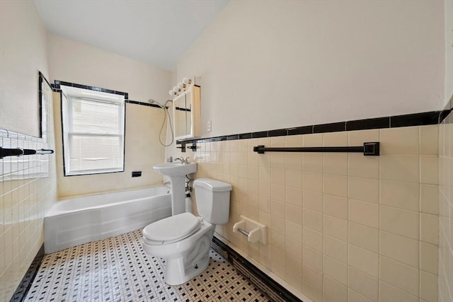 bathroom with shower / bath combination, tile walls, toilet, and a wainscoted wall