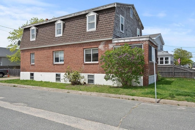 view of home's exterior featuring mansard roof, brick siding, and fence