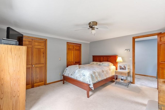 bedroom with light colored carpet, baseboards, multiple closets, and a ceiling fan