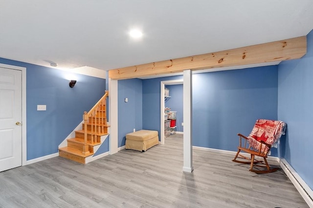 finished below grade area with baseboard heating, wood finished floors, stairs, and baseboards