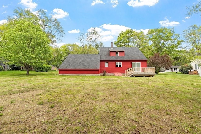 rear view of house with a deck, a lawn, roof with shingles, and a chimney