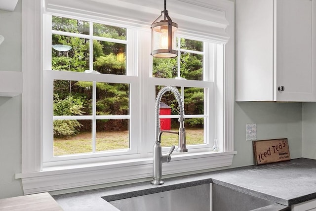 kitchen view of a sink, white cabinetry, and pendant lighting