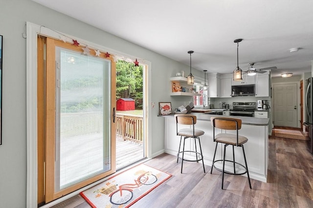 kitchen featuring appliances with stainless steel finishes, a peninsula, white cabinets, wood finished floors, and a kitchen bar