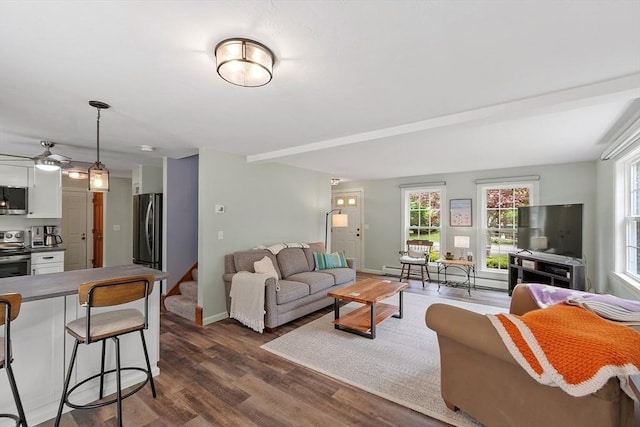 living room featuring baseboard heating, plenty of natural light, dark wood-style floors, and a ceiling fan