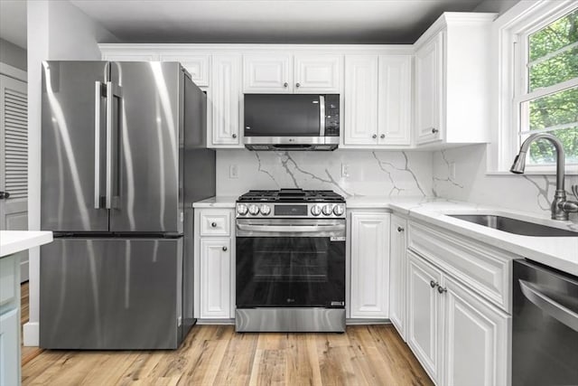 kitchen with stainless steel appliances, a sink, white cabinetry, decorative backsplash, and light wood-style flooring
