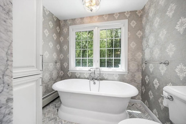 full bath featuring toilet, a baseboard radiator, a soaking tub, and baseboards