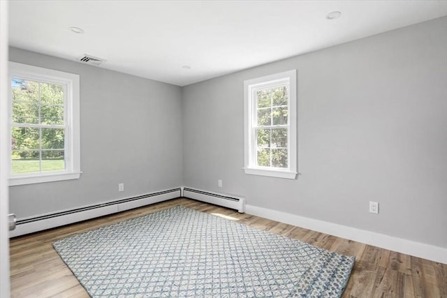 empty room with plenty of natural light, a baseboard radiator, baseboards, wood finished floors, and recessed lighting
