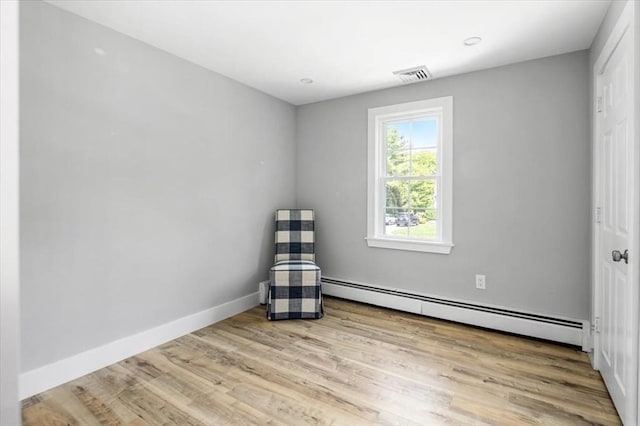 empty room with a baseboard radiator, wood finished floors, and baseboards
