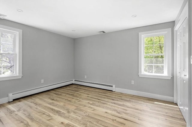 spare room with a baseboard radiator, light wood-type flooring, and baseboards