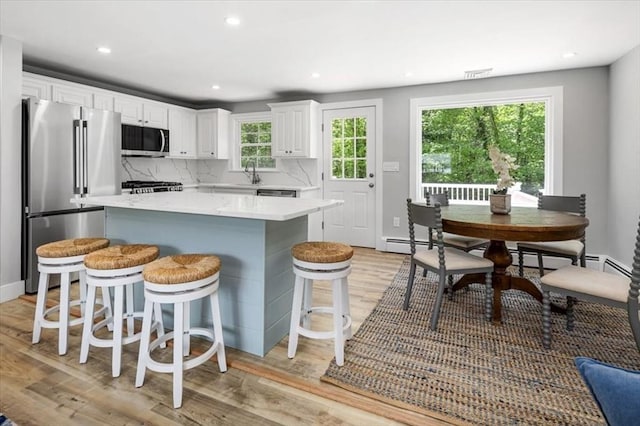 kitchen featuring stainless steel appliances, light wood-style floors, white cabinets, a breakfast bar area, and a center island