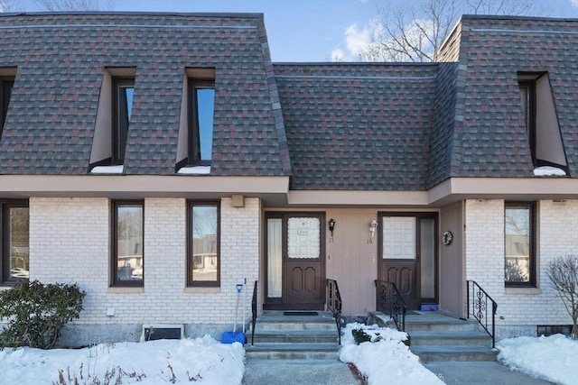 view of property with mansard roof, roof with shingles, and brick siding