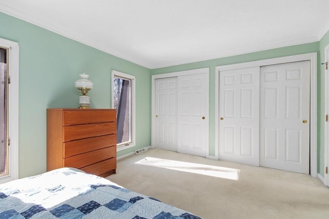 bedroom with two closets, visible vents, ornamental molding, light carpet, and baseboards