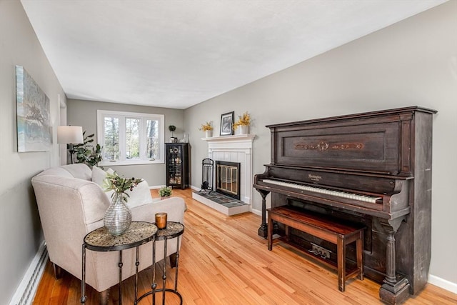living room with baseboards, a baseboard radiator, light wood-style flooring, and a tile fireplace