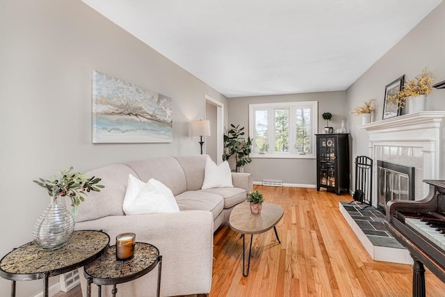 living room with baseboards, visible vents, a tiled fireplace, and light wood finished floors