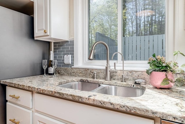 interior details featuring a sink, decorative backsplash, white cabinets, and light stone countertops