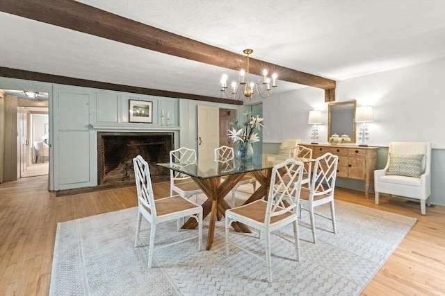 dining area with a chandelier, beamed ceiling, and light wood-type flooring