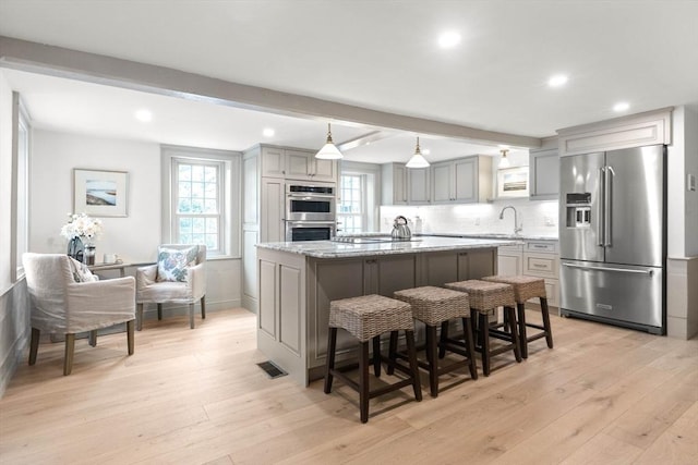 kitchen featuring appliances with stainless steel finishes, gray cabinetry, beam ceiling, light stone counters, and a kitchen island