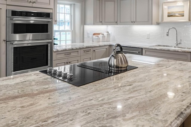 kitchen with tasteful backsplash, light stone countertops, appliances with stainless steel finishes, and sink