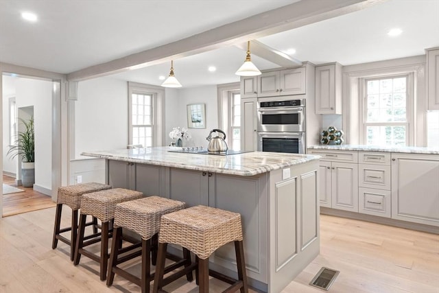 kitchen featuring gray cabinetry, double oven, light stone counters, and a center island