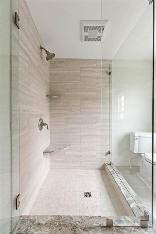 bathroom featuring a shower with door and toilet