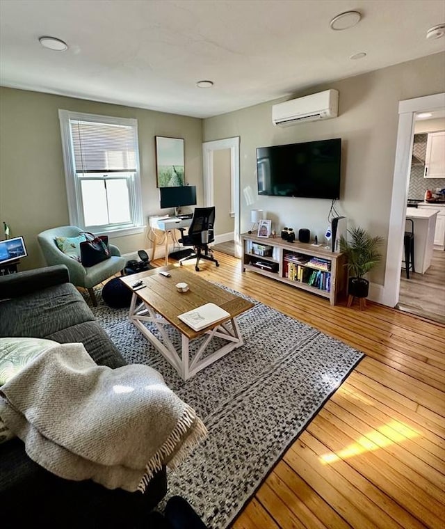 living area featuring light wood-type flooring, a wall mounted air conditioner, and baseboards