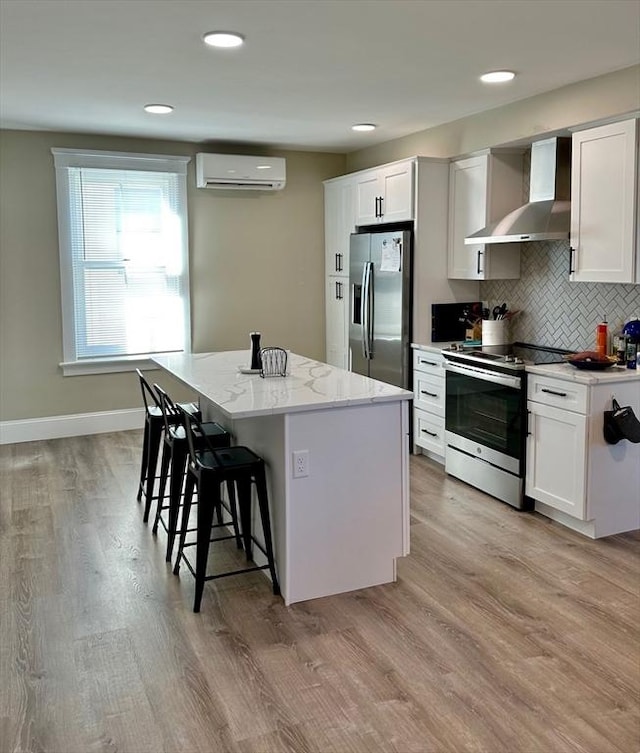 kitchen featuring wall chimney exhaust hood, stainless steel appliances, an AC wall unit, a kitchen island, and a kitchen breakfast bar