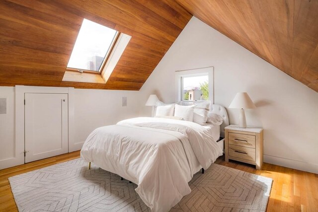 bedroom with vaulted ceiling with skylight, light wood finished floors, wood ceiling, and baseboards